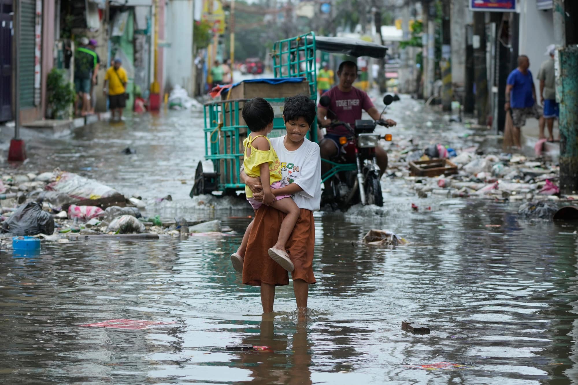 A woman and child crosses a flooded street due to Typhoon Fung-wong and high tide on Monday, Nov. 10, 2025, in Navotas, Philippines